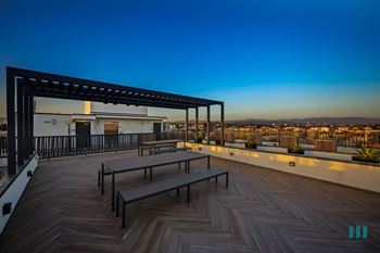 Rooftop deck entertainment area  and a pergola is set against a sunset sky.